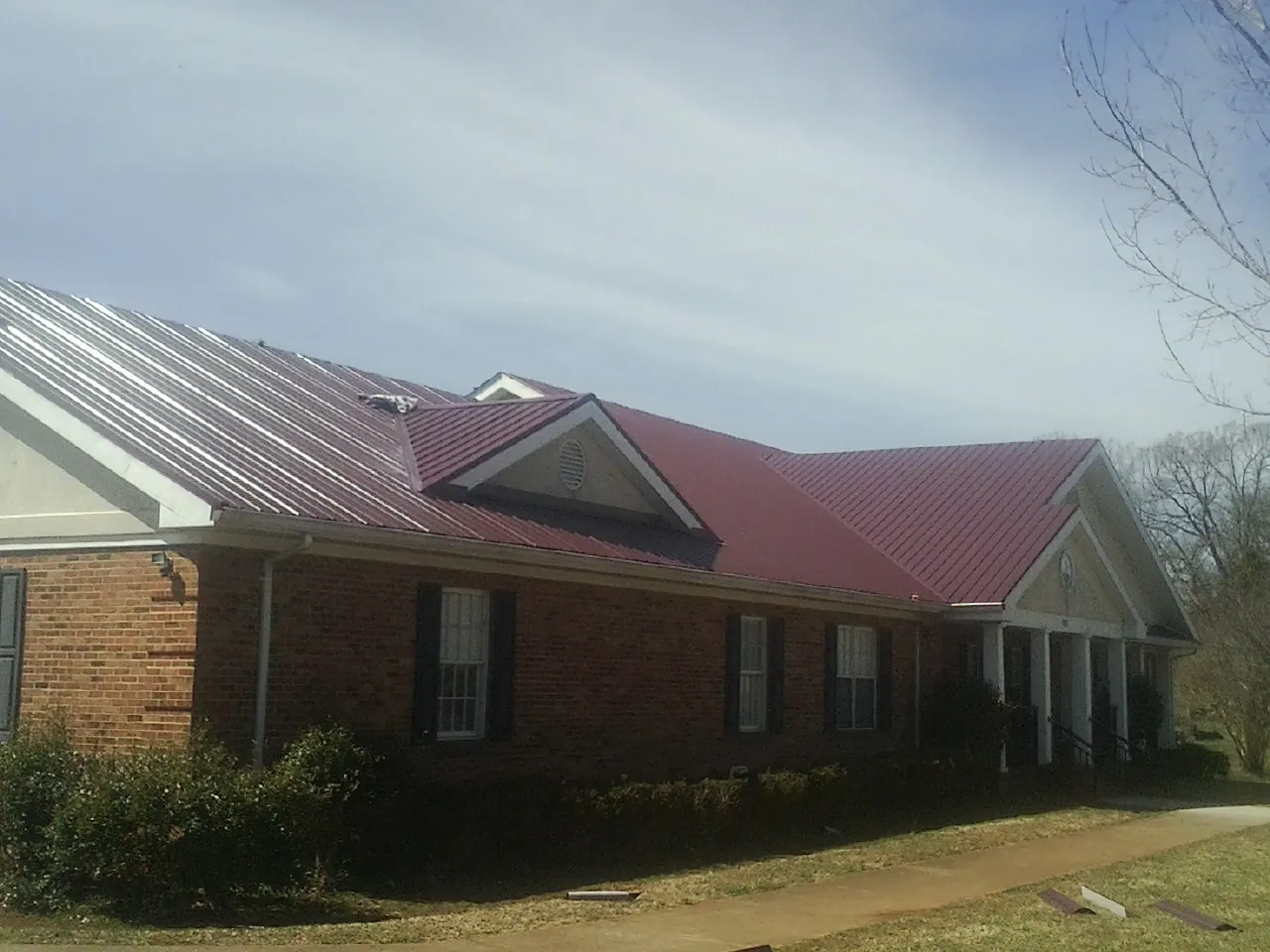 Red metal roof with gabled entries on a long brick building, from a Hail Damage Roof Repair job in Palmersville