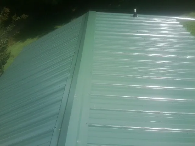 New green metal panels meeting at the ridge of a roof — Flat Roof Repair work by our crew in Palmersville