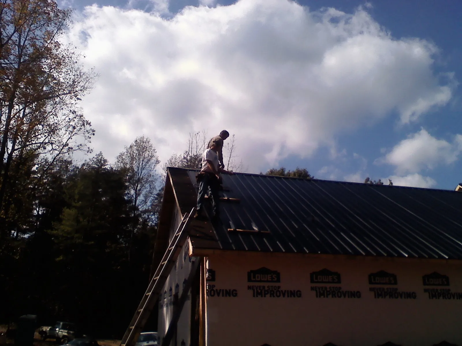 Roofer fastening dark metal panels high against a cloudy sky, from a Roof Inspection job in Palmersville