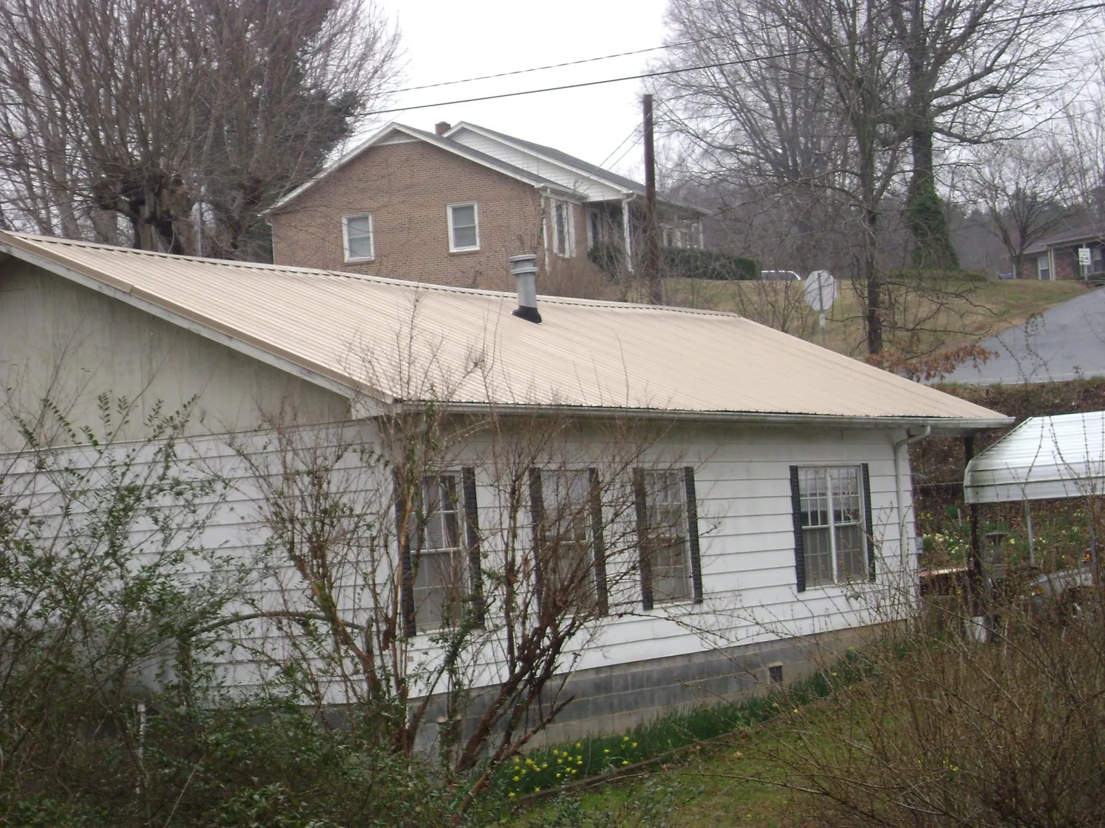 Tan metal roof on a white sided house set into a hillside — Commercial Roofing by Roofing Brothers in Palmersville