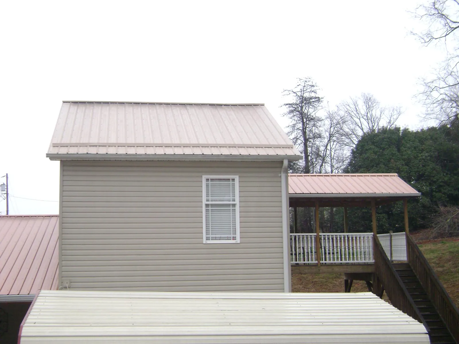 Tan metal roofs on a two story addition and attached porch, from a Roof Replacement job in Palmersville